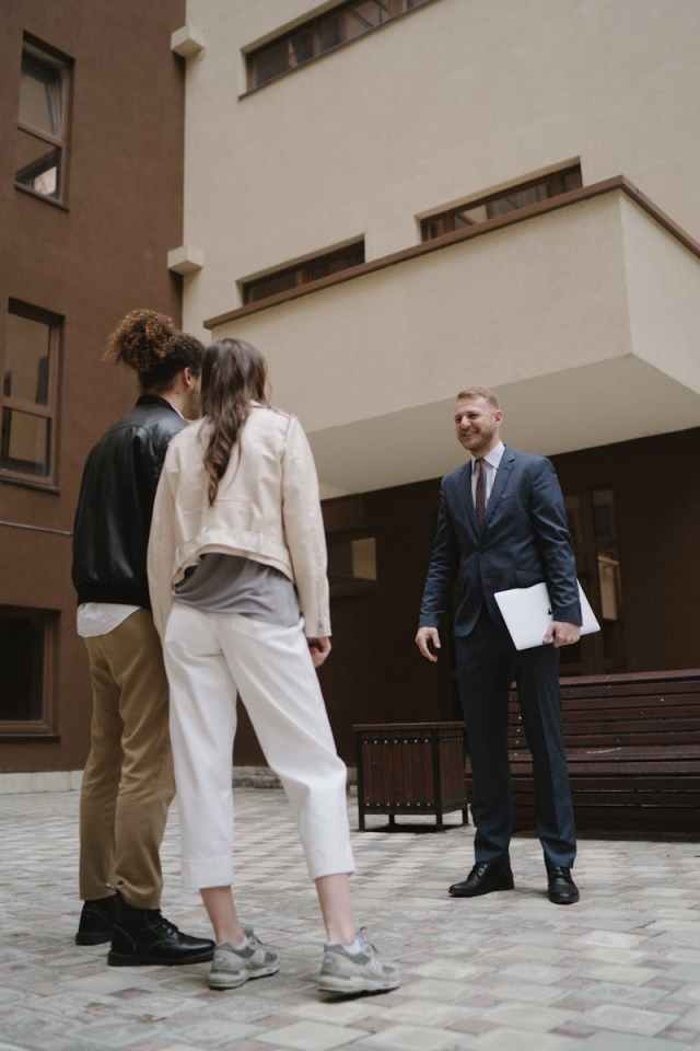 A professional realtor showing a new apartment to a young couple in a city setting.