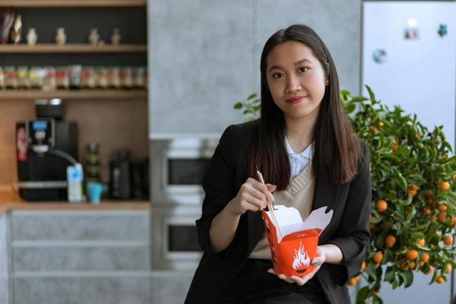 Businesswoman enjoys a quick lunch with Asian noodles in a modern office setting.