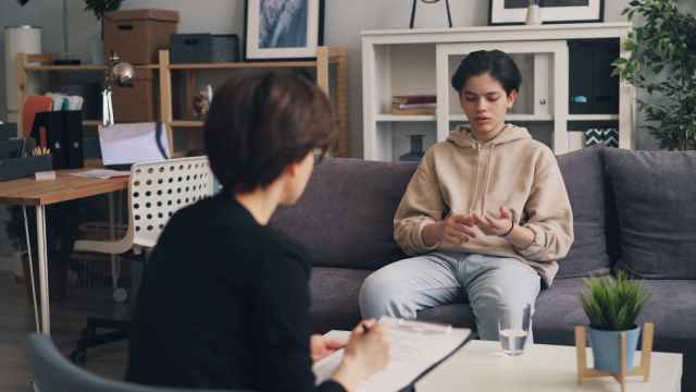 A teenager engages in a therapy session with a professional counselor in a modern office setting.