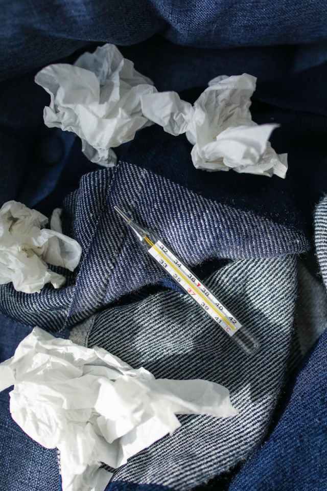 Used tissues and a thermometer on denim, symbolizing illness at home.
