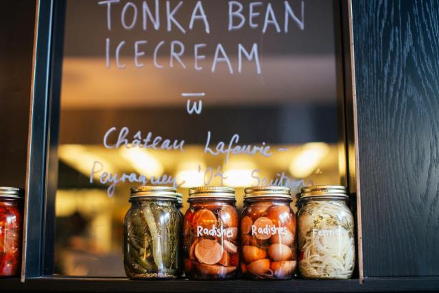 Mason jars with vegetables on café shelf; handwritten menu on glass.