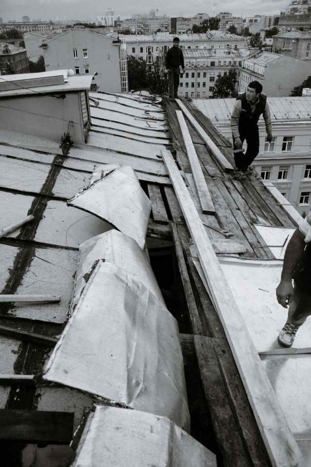 A group of workers repairing a damaged urban rooftop from a high angle.
