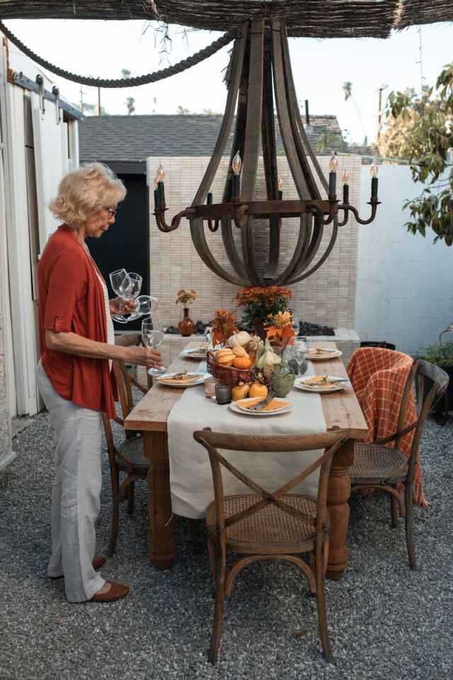 An elegant outdoor Thanksgiving dinner setup with a senior woman arranging the table.