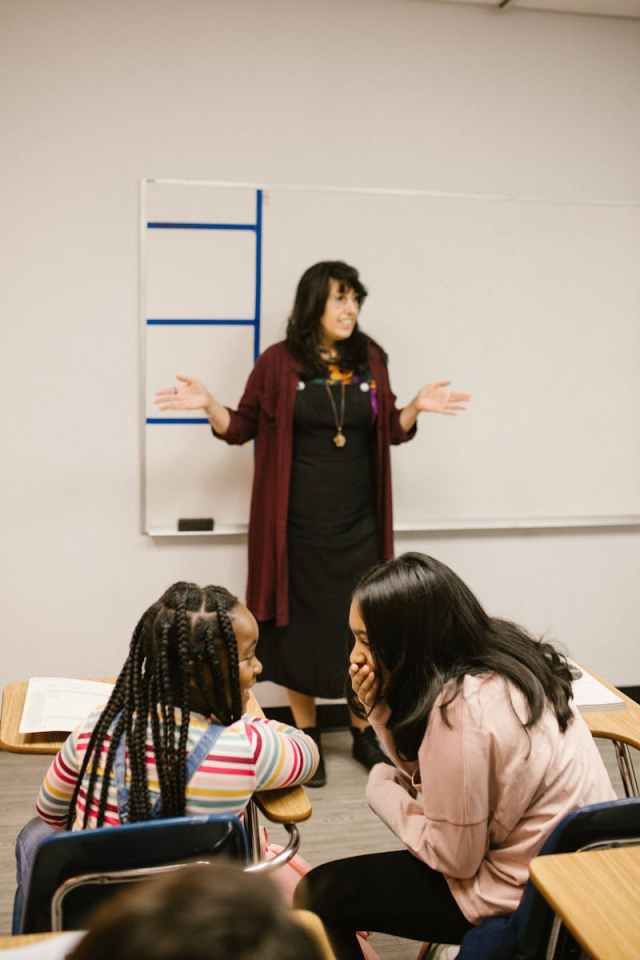 Teacher leading classroom discussion with students at their desks.