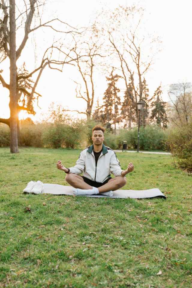 Man meditating on yoga mat in park, surrounded by nature, during sunrise.