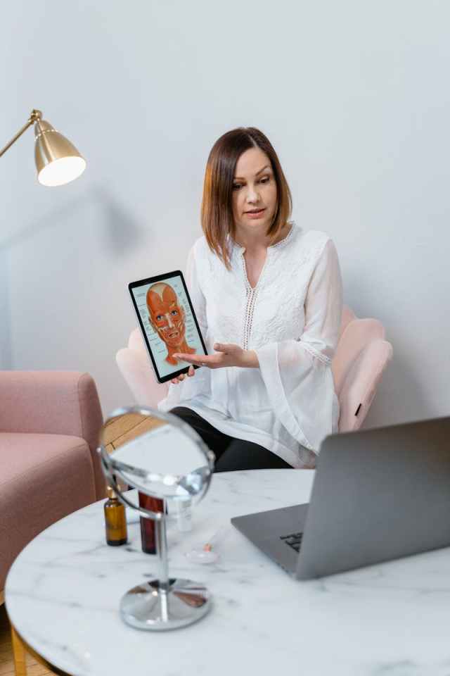 A woman demonstrates a skincare routine using digital tools during an online consultation.