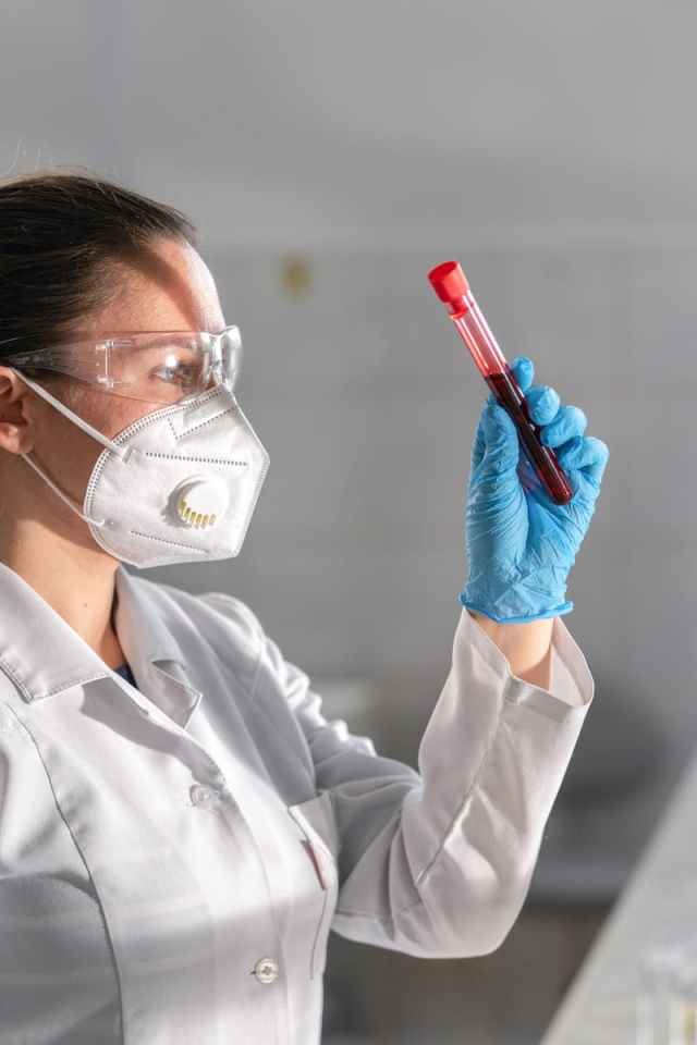 A female scientist in protective gear examines a blood sample in a laboratory setting.