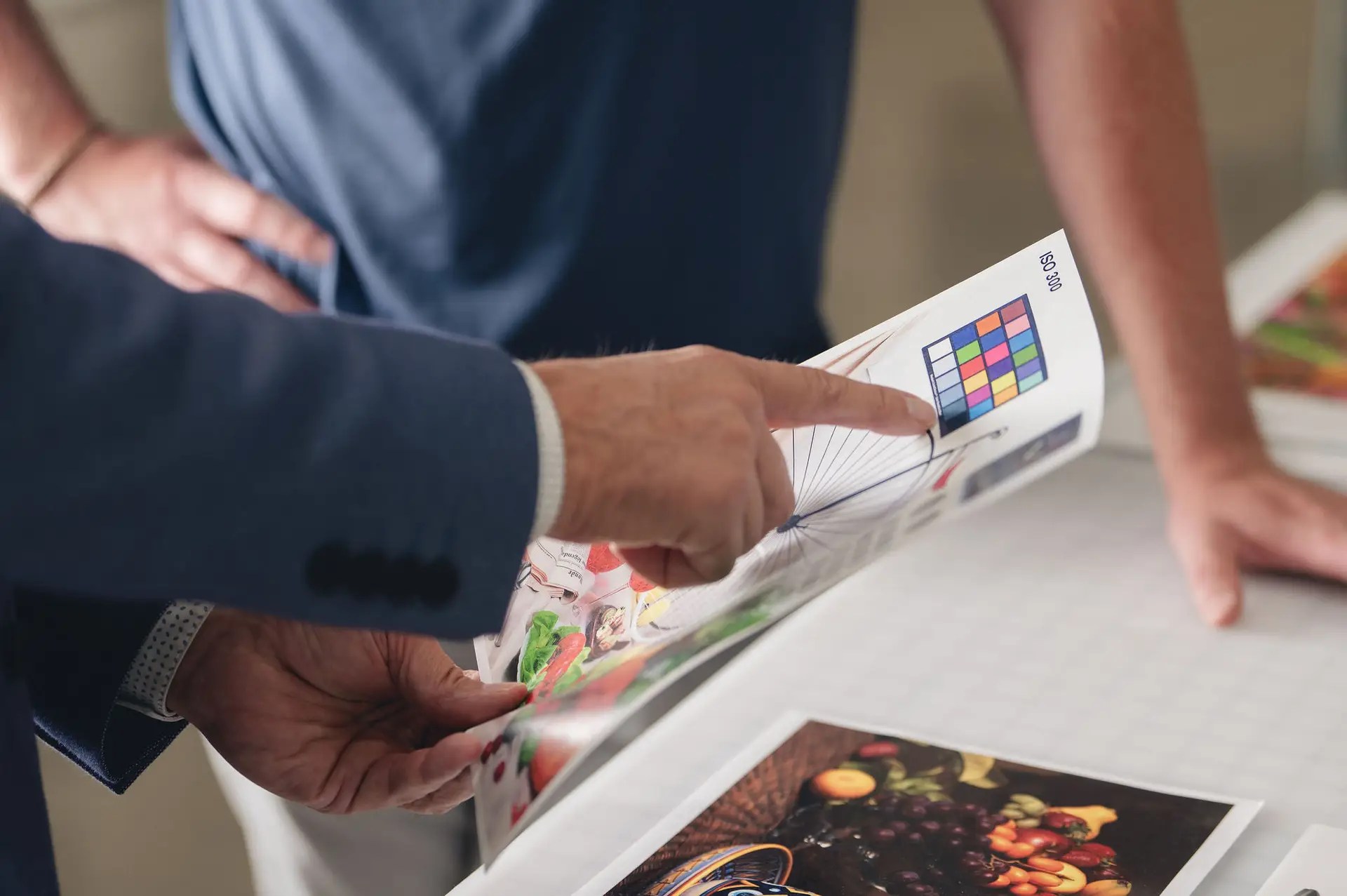 Two people review a printed sheet with colorful images and a color calibration chart. One points to the chart while the other stands nearby, both focused on print quality—a testament to expert production print services in Ohio.