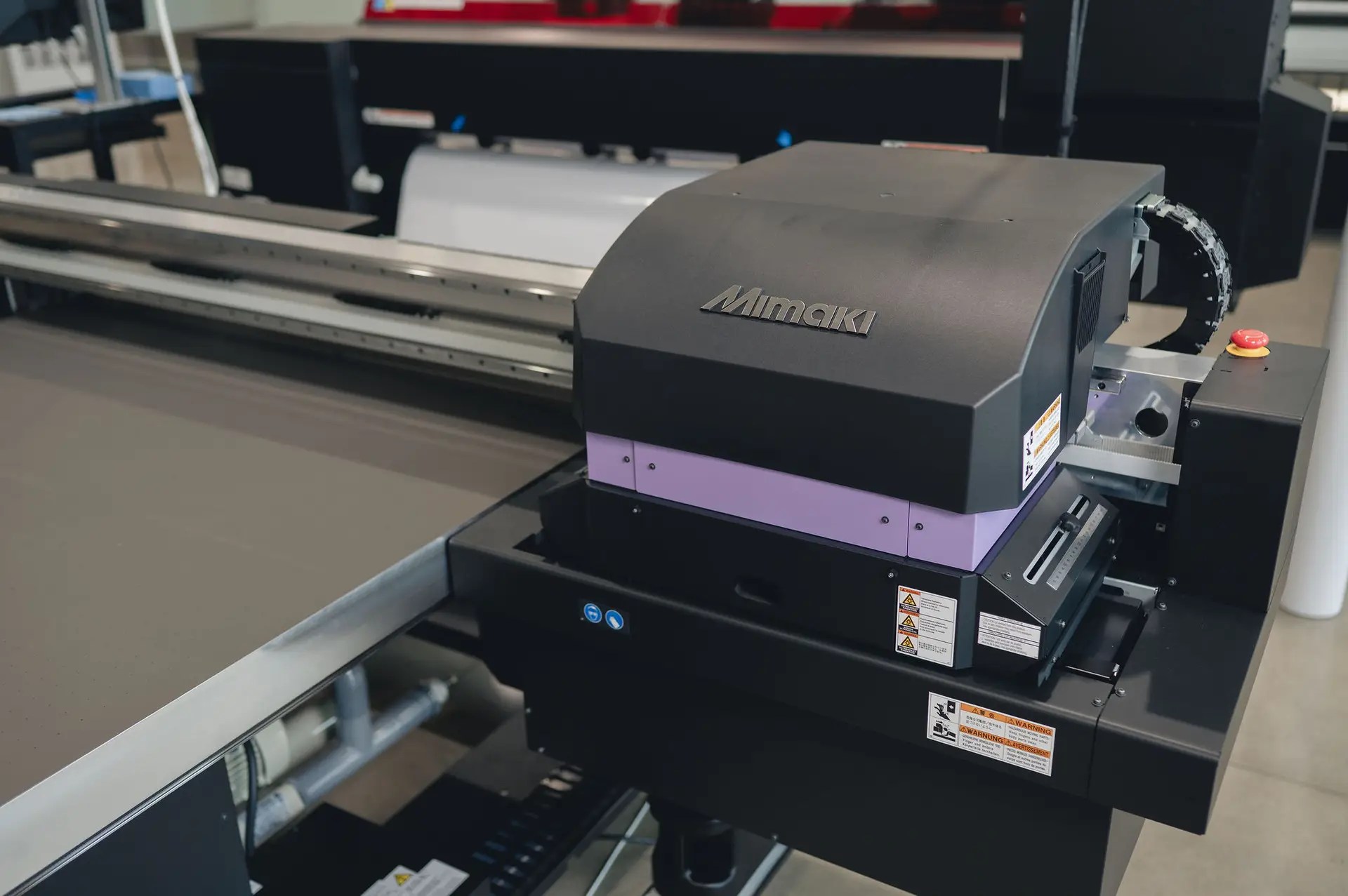 A close-up of a Mimaki flatbed printer in a workspace, featuring the control panel, warning labels, and printing surface. This black printer with a purple accent is ready for operation—ideal for those seeking top printers and copiers in Ohio.