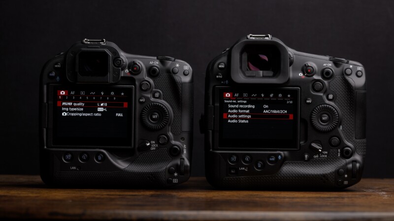 Two professional DSLR cameras are placed side by side on a wooden surface, with screens displaying menu settings for image quality and sound recording. The cameras have a textured grip and multiple buttons, knobs, and dials.