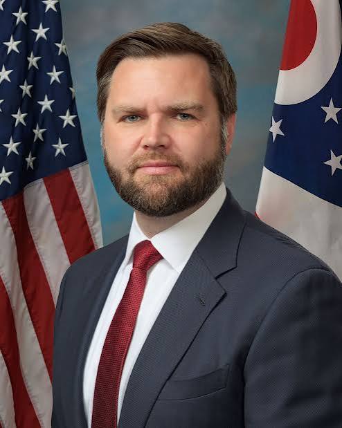 Portrait of a man in a dark suit and red tie in front of the US and Ohio flags