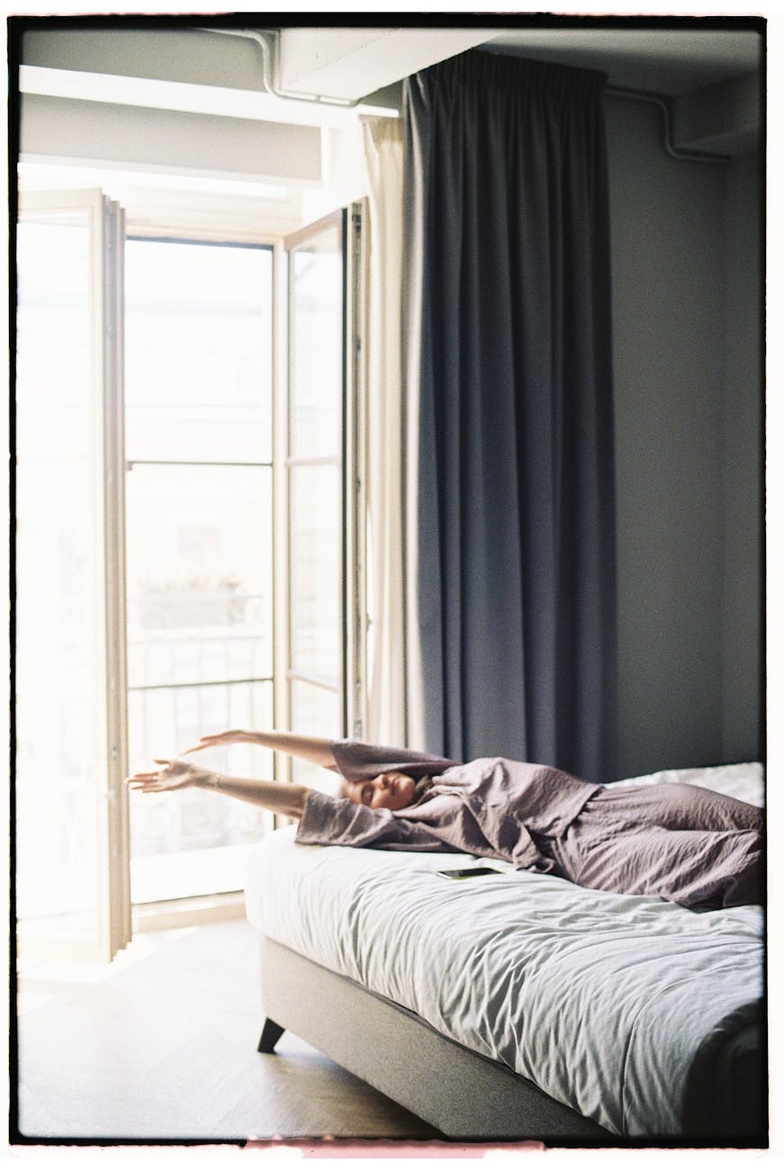 woman stretching on bed near balcony door