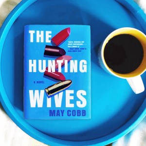 The Hunting Wives by May Cobb is a blue book with lipstick and a bullet on the cover. This book is a dark, dramatic fiction thriller that is being adapted for television.