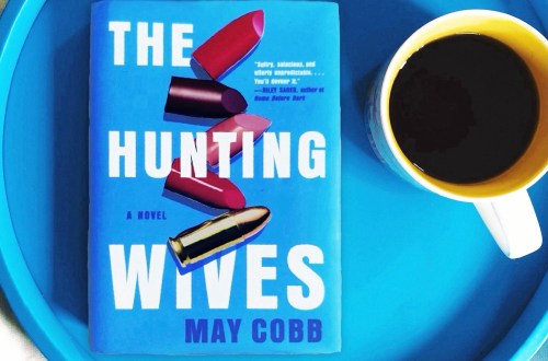 The Hunting Wives by May Cobb is a blue book with lipstick and a bullet on the cover. This book is a dark, dramatic fiction thriller that is being adapted for television.