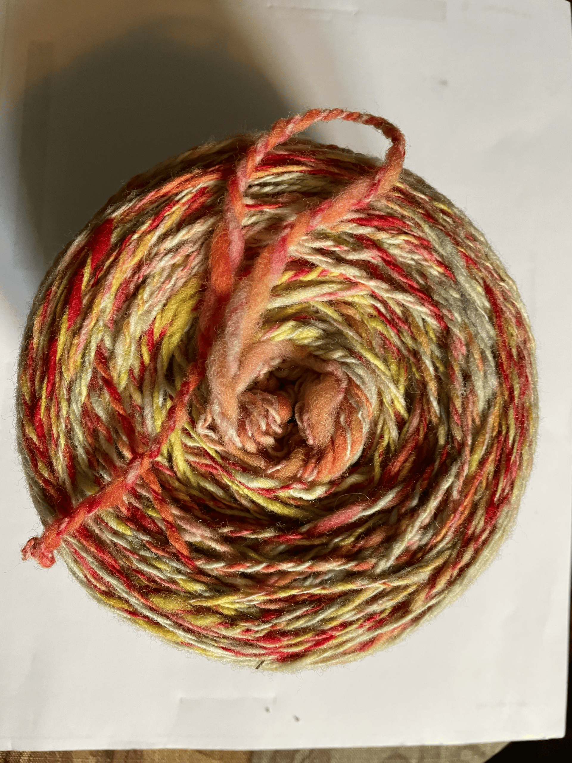A spiral of handspun yarn in warm coral, gold and earthy tones.