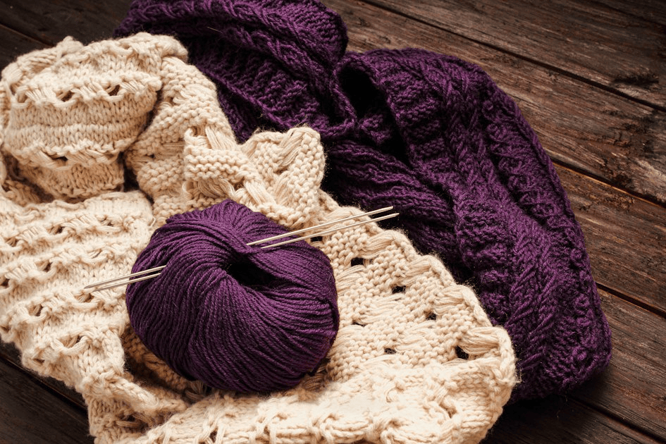A ball of purple yarn resting on cream and purple textured knitting.