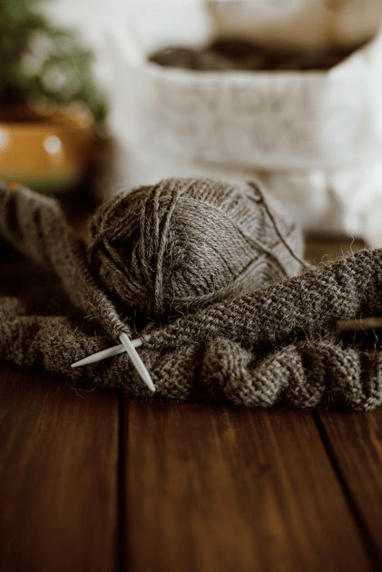 A ball of brown yarn and knitting needles beside a knitted piece on a wooden table.