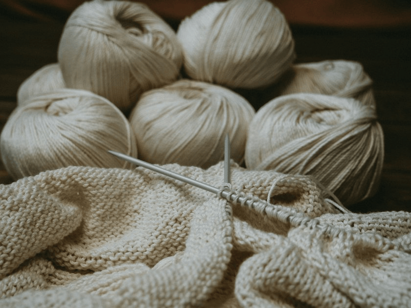 Balls of cream yarn beside a partially knitted piece and needles.