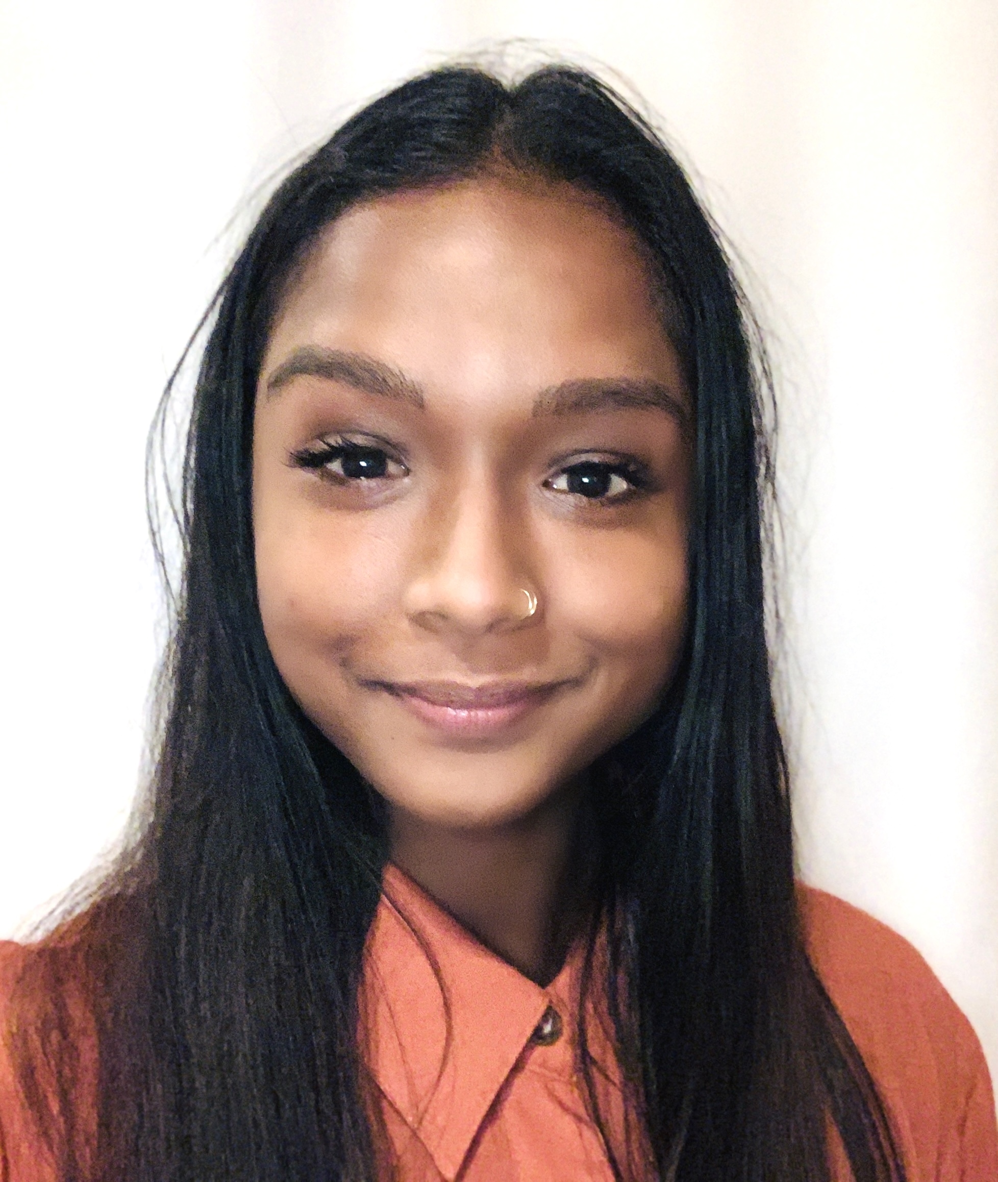 A headshot photo of Whitney Hosein, a young brown woman with straight black hair wearing an orange button-up shirt.
