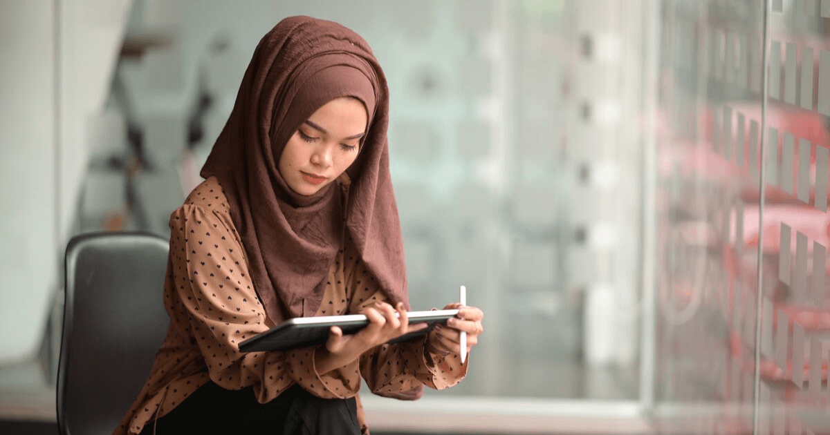 A woman openly wears a hijab while working on a tablet as her workplace has guidelines to help accomodate her religious beliefs