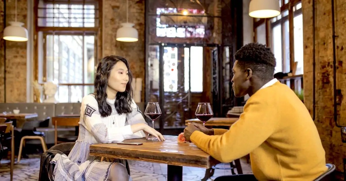 two people sitting at a table inside of a restaurant on a first date with one person oversharing too soon their personal information a no no for first date etiquette