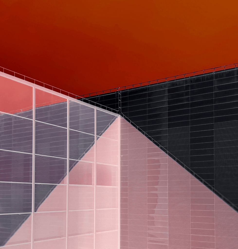 Vista abstracta de un edificio con paredes de cristal y colores en tonos rojo, rosa y negro, creando un contraste geométrico.