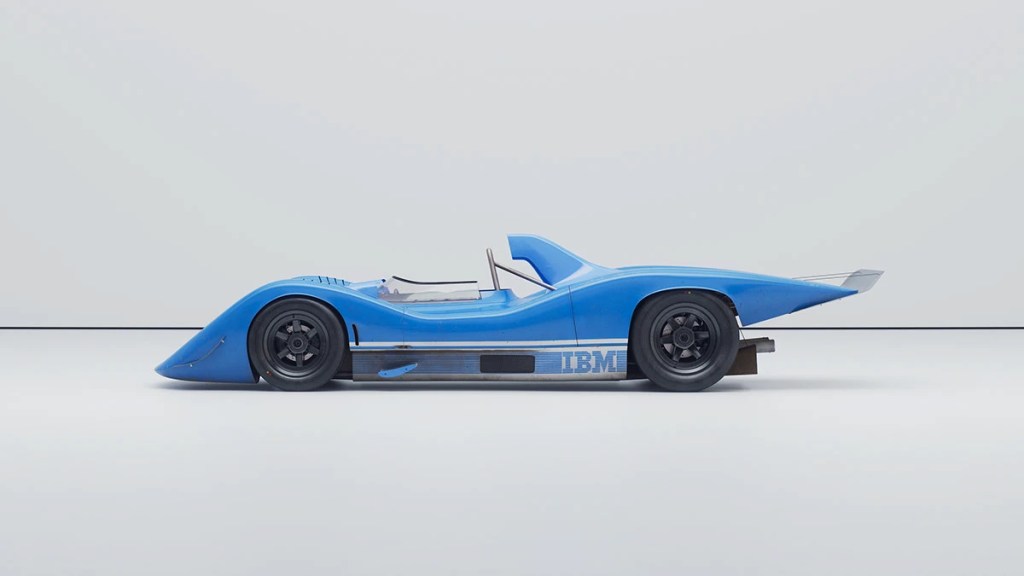 Vista lateral de un coche de carreras azul con un diseño aerodinámico, presentado contra un fondo blanco liso.