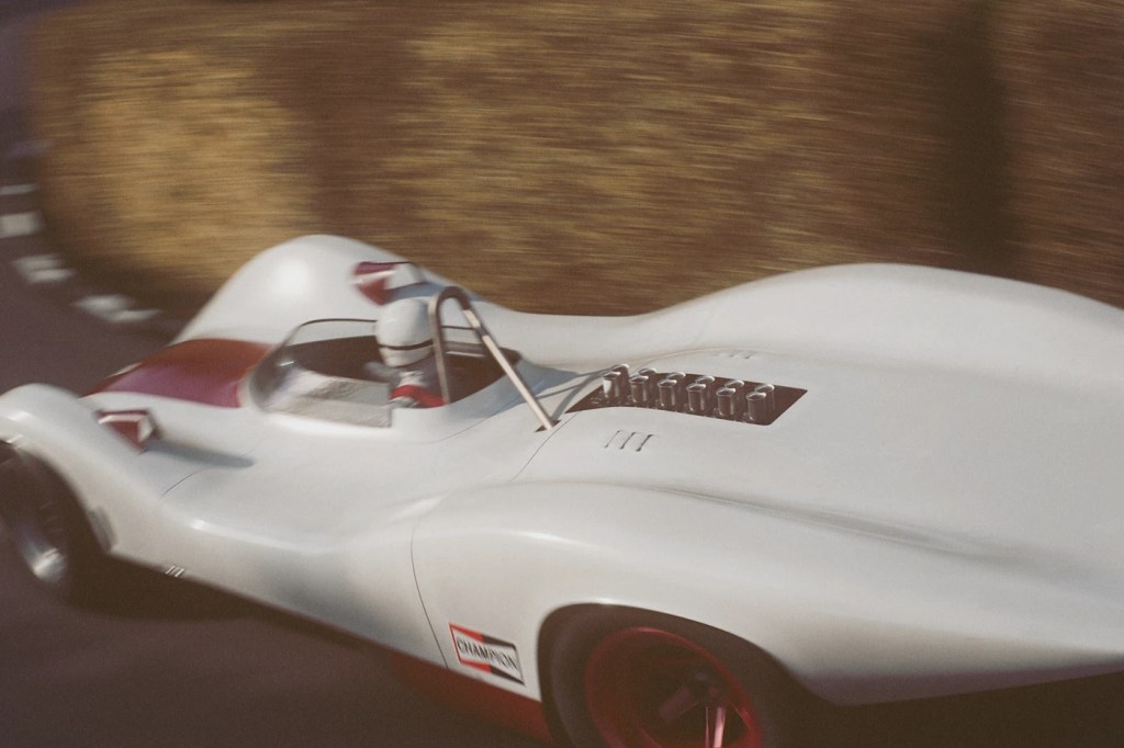 Un coche de carreras de diseño futurista en movimiento, con un piloto visible y un fondo desenfocado que sugiere velocidad.