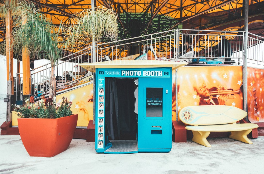 Cabina de fotos azul en un parque de atracciones, rodeada de plantas y decoraciones coloridas.