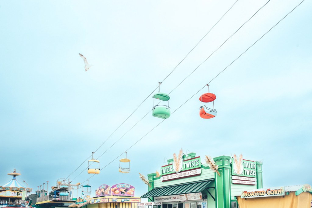 Vista de un parque de diversiones con góndolas de colores suspendidas sobre una zona de comida.