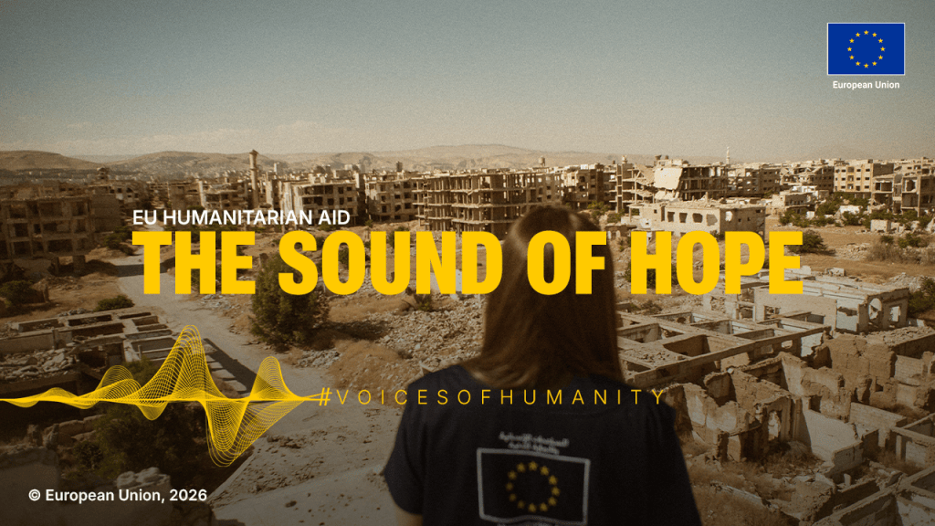Imagen que muestra una vista de un área devastada, con edificios en ruinas y una persona de espaldas vistiendo una camiseta que representa la ayuda humanitaria de la Unión Europea. En primer plano, se destaca el texto 'THE SOUND OF HOPE' y el hashtag '#VOICESOFHUMANITY'.