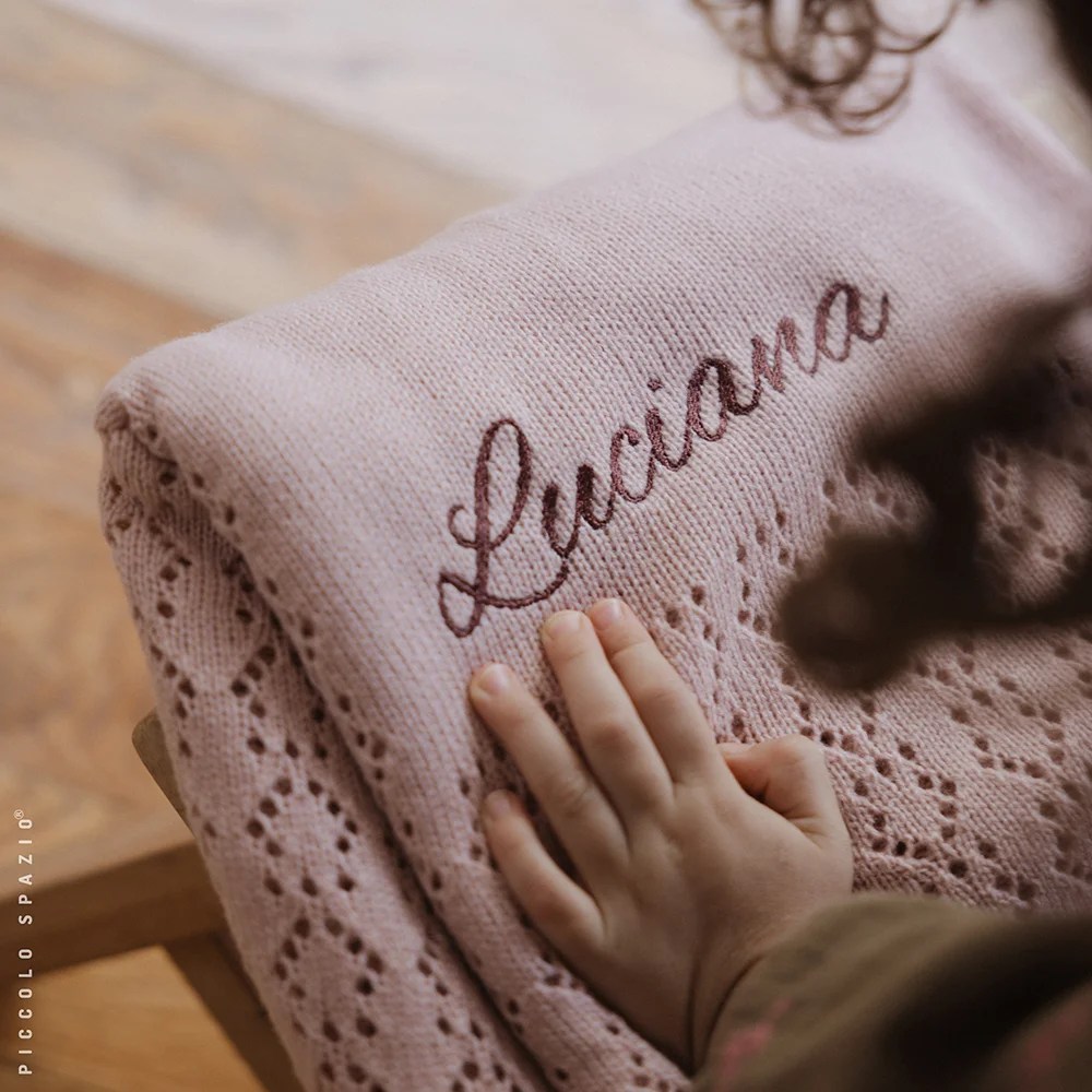 Frazada para bebé color rosa personalizada sobre una banca mientras una niña la acaricia-Piccolo Spazio