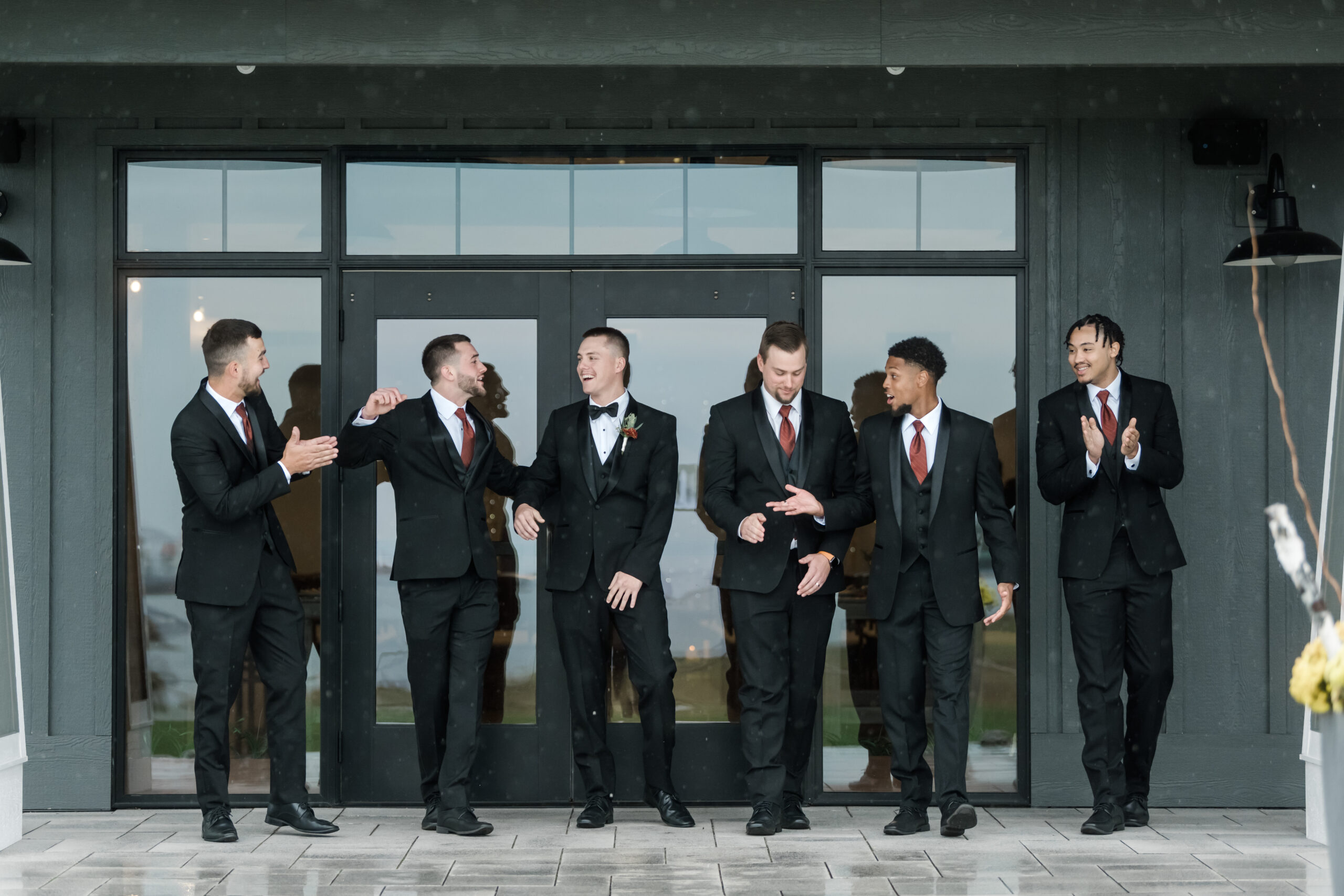 Groom and his groomsmen in black and terracotta tuxedos outside of a wedding venue in Saugatuck, Michigan. The groom and groomsmen rented their tuxedos from Pierre's Bridal, Prom, and Tuxedo in Lansing, Michigan.