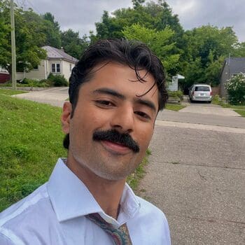 Kamil Ahmed smiling for his headshot with a community setting in the background