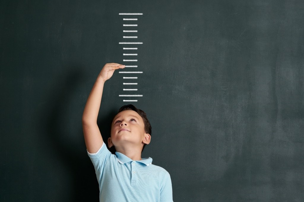Little boy standing in front of chalkboard to measure his height