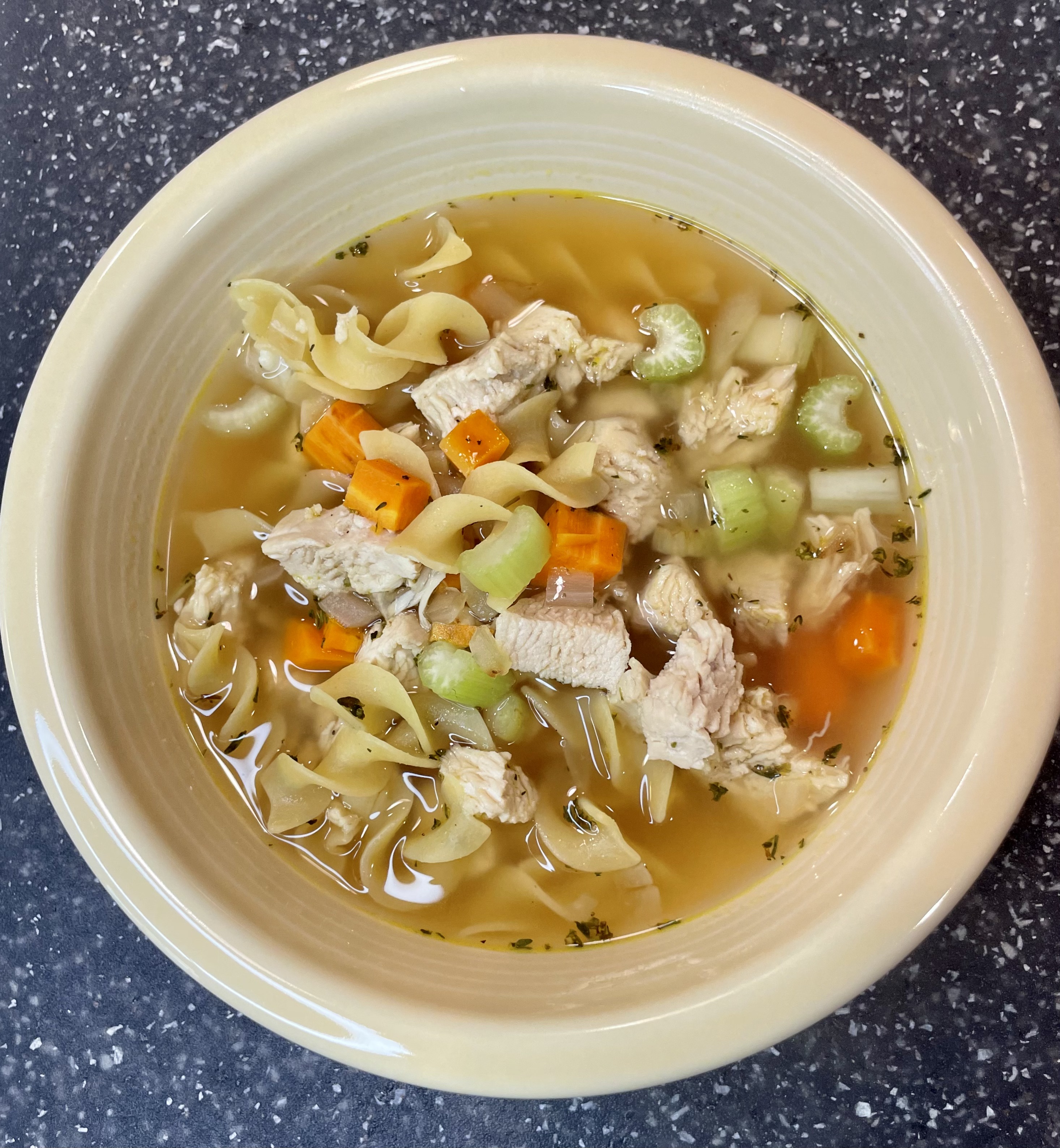 Chicken noodle soup in a creamy colored bowl.