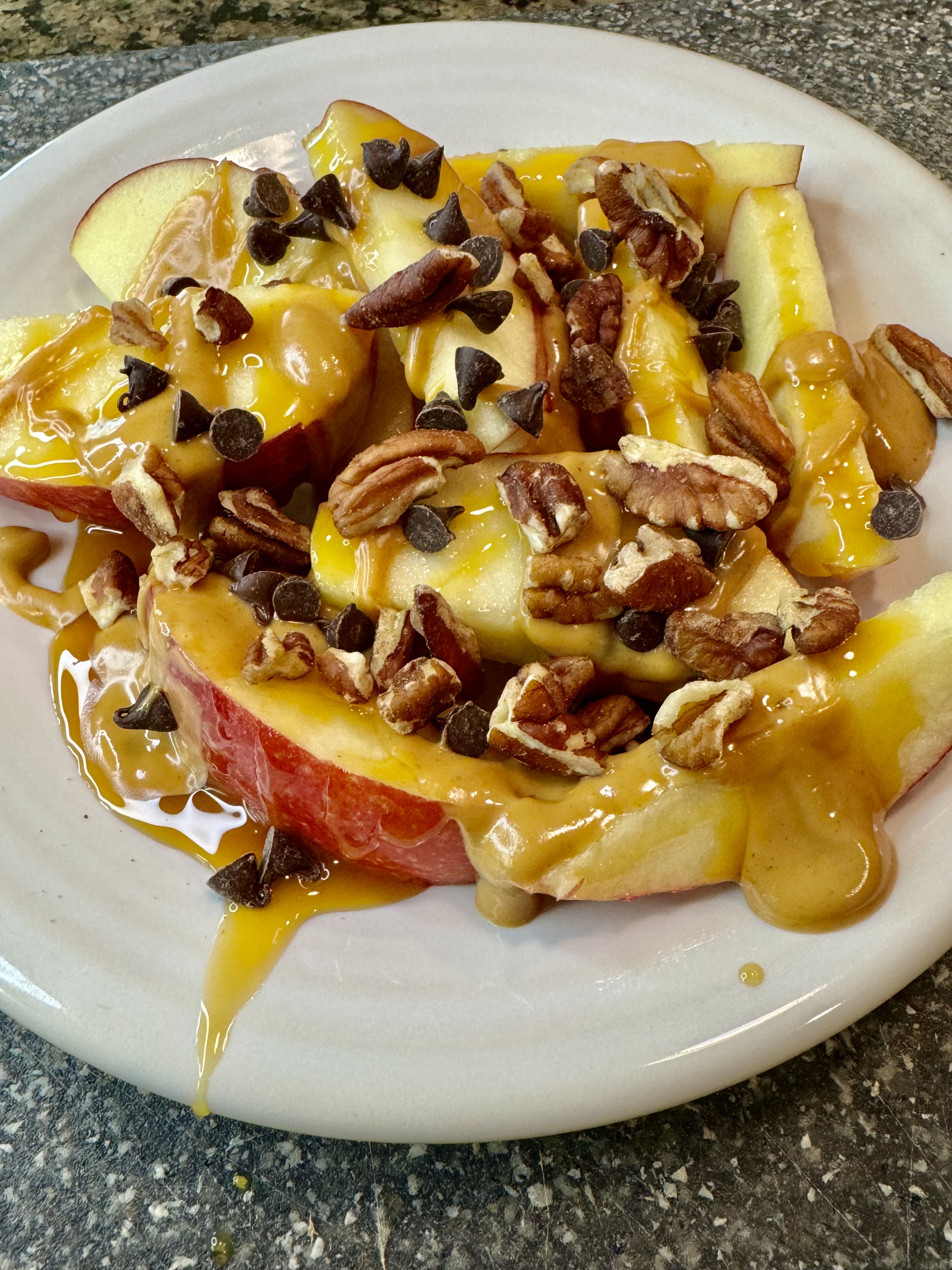 Apple nachos on a white plate with caramel drizzle and chocolate chips.