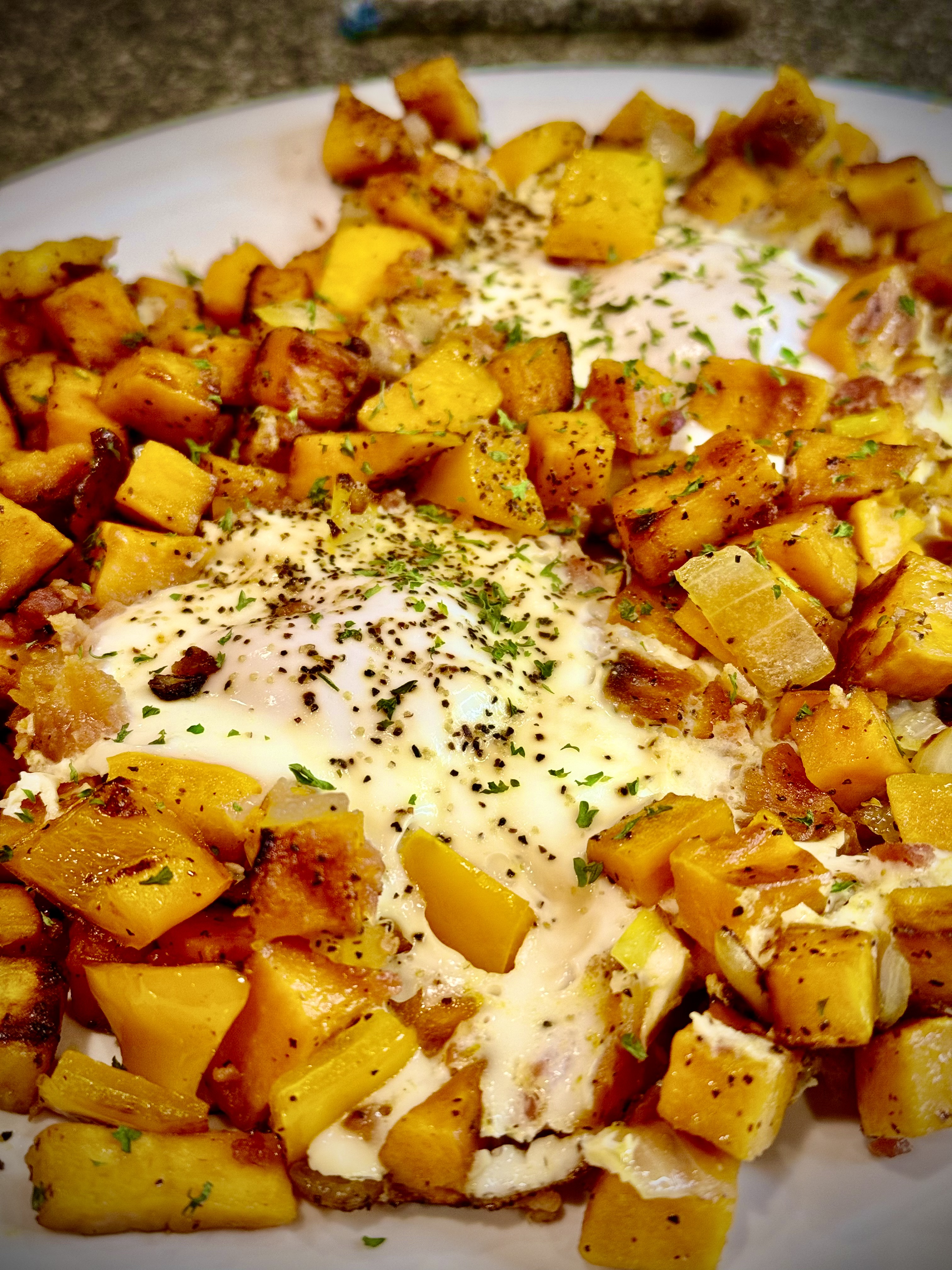 Sweet potato breakfast hash with diced sweet potatoes, crispy bacon, bell peppers, onions, and fried eggs on top.