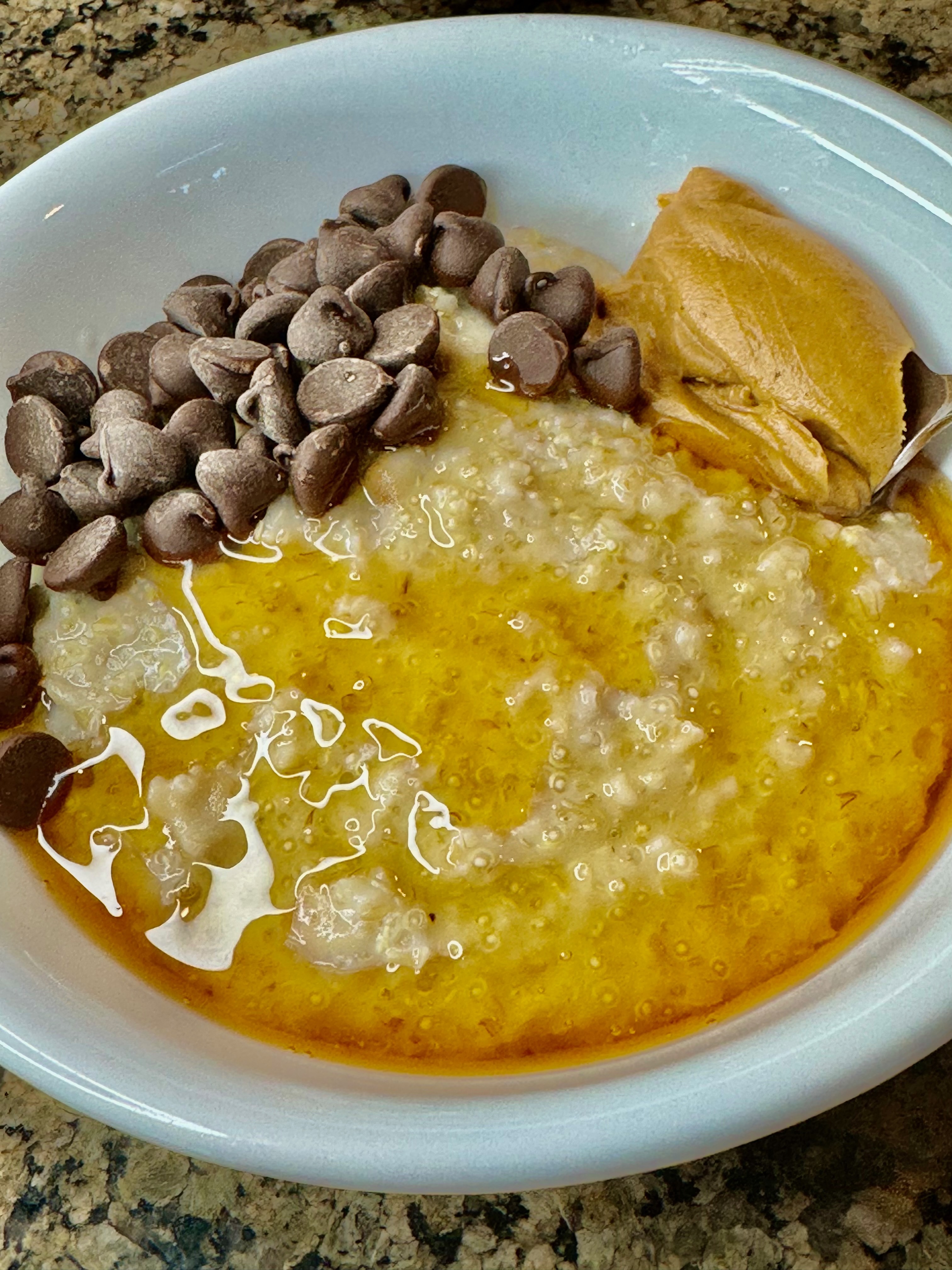 A steel cut oats and quinoa bowl topped with chocolate chips, peanut butter, and drizzled with honey.