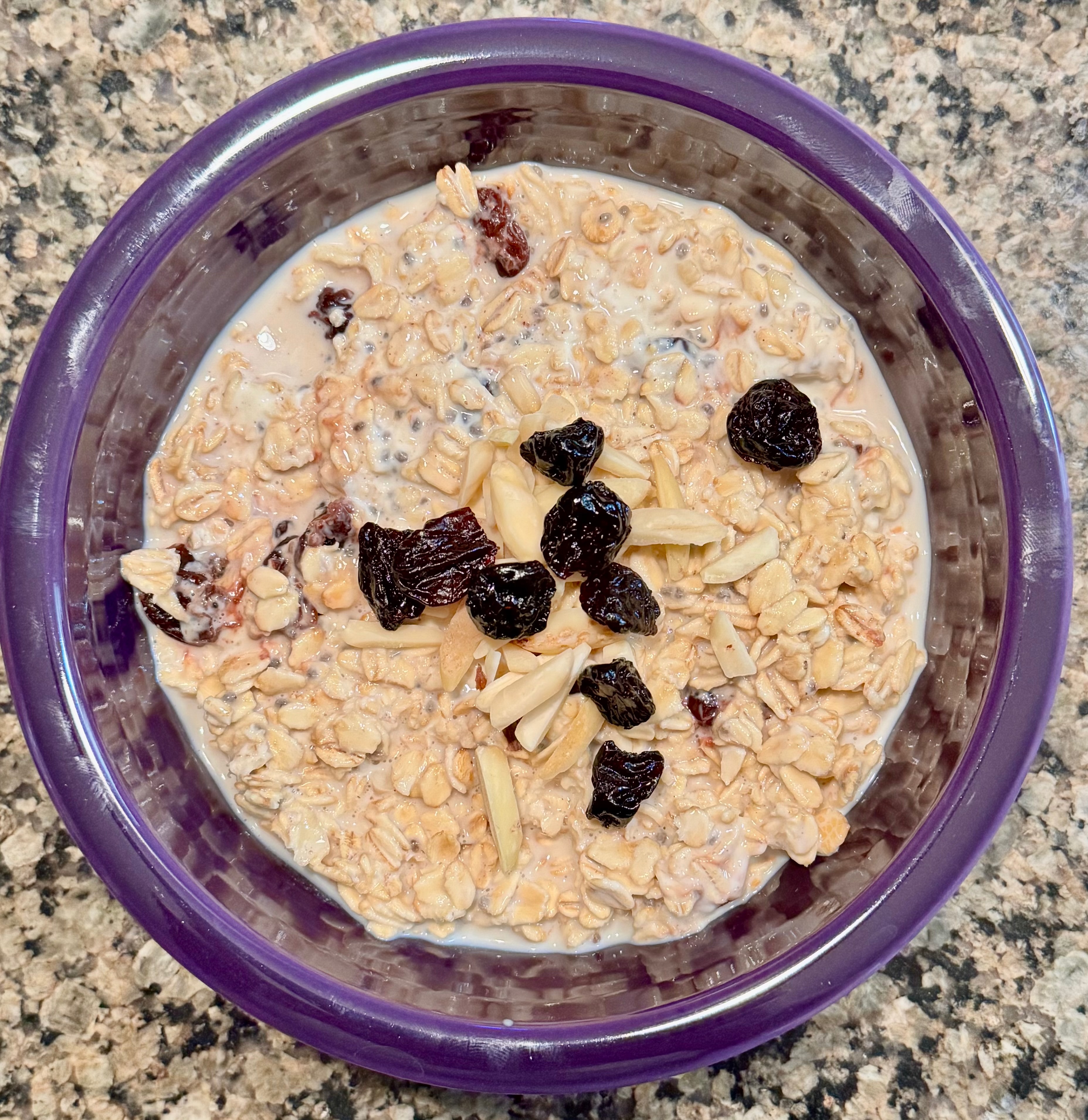 Purple bowl of cherry almond cake overnight oats topped with slivered almonds and dried cherries