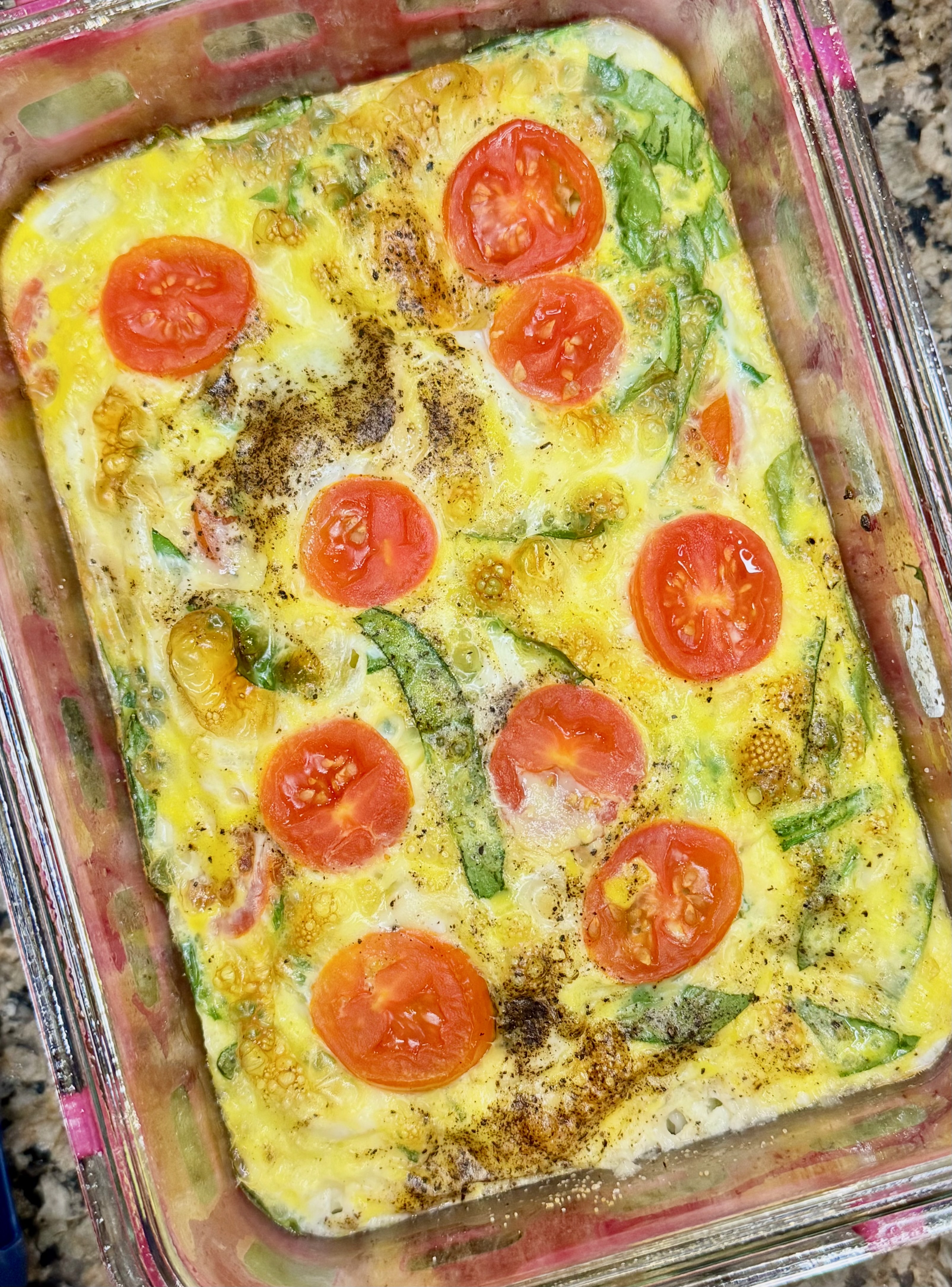 Spinach and tomato egg bowl in a glass meal prep container.