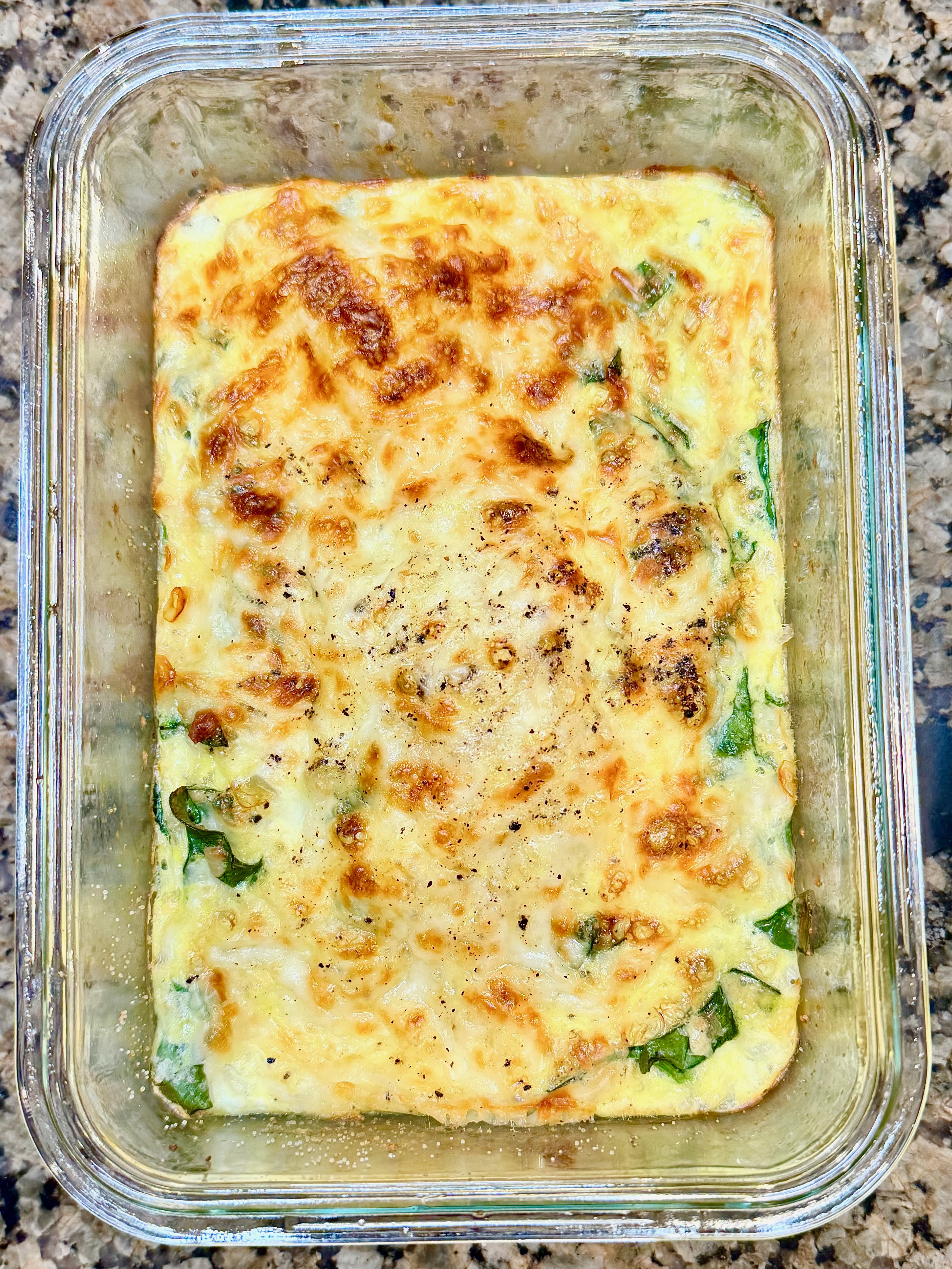 Spinach and artichoke egg bowl topped with melted mozzarella in a glass dish.