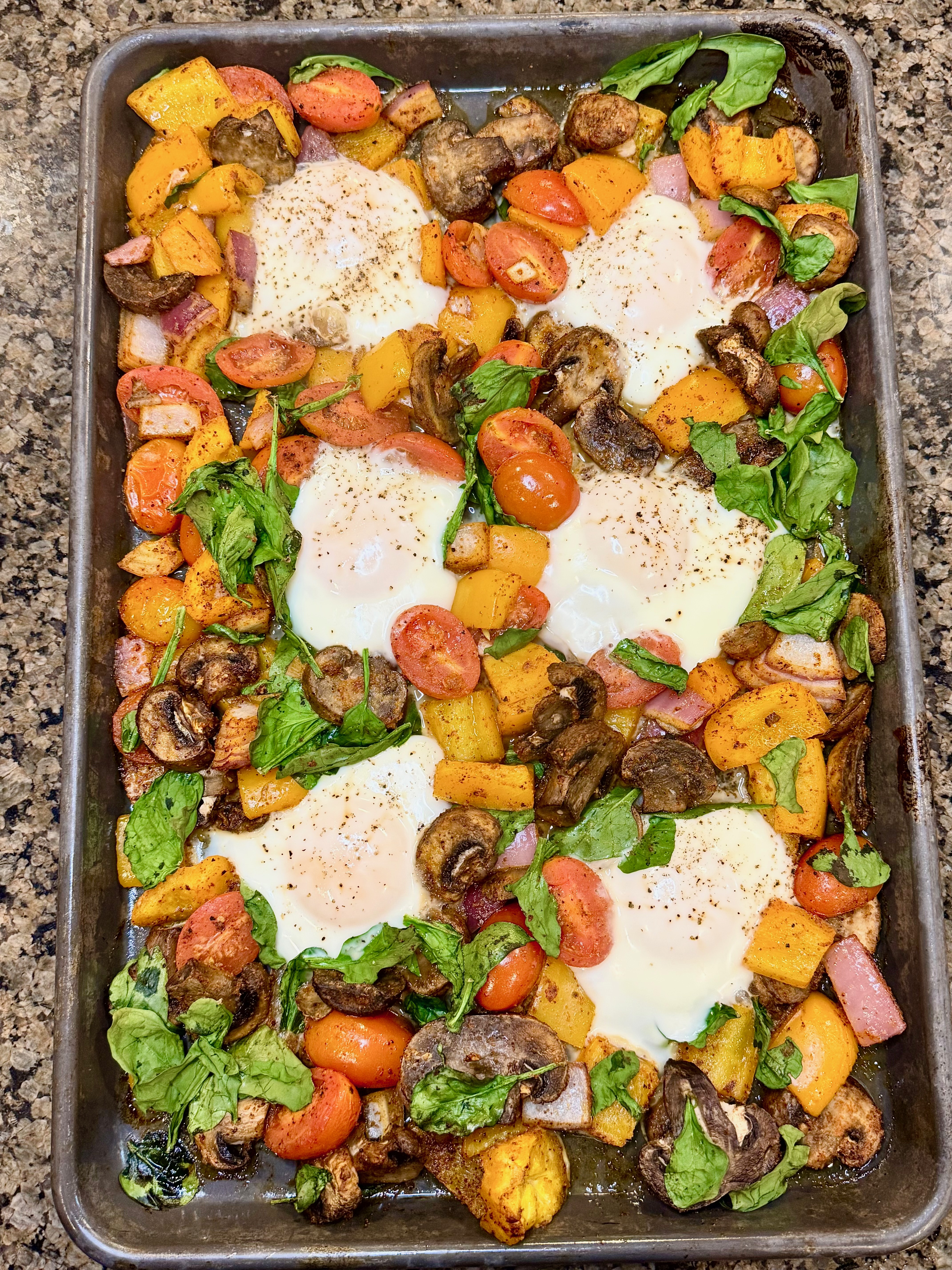 A breakfast sheet pan meal with roasted sweet potatoes, sautéed mushrooms, spinach, and baked eggs, served fresh from the oven.