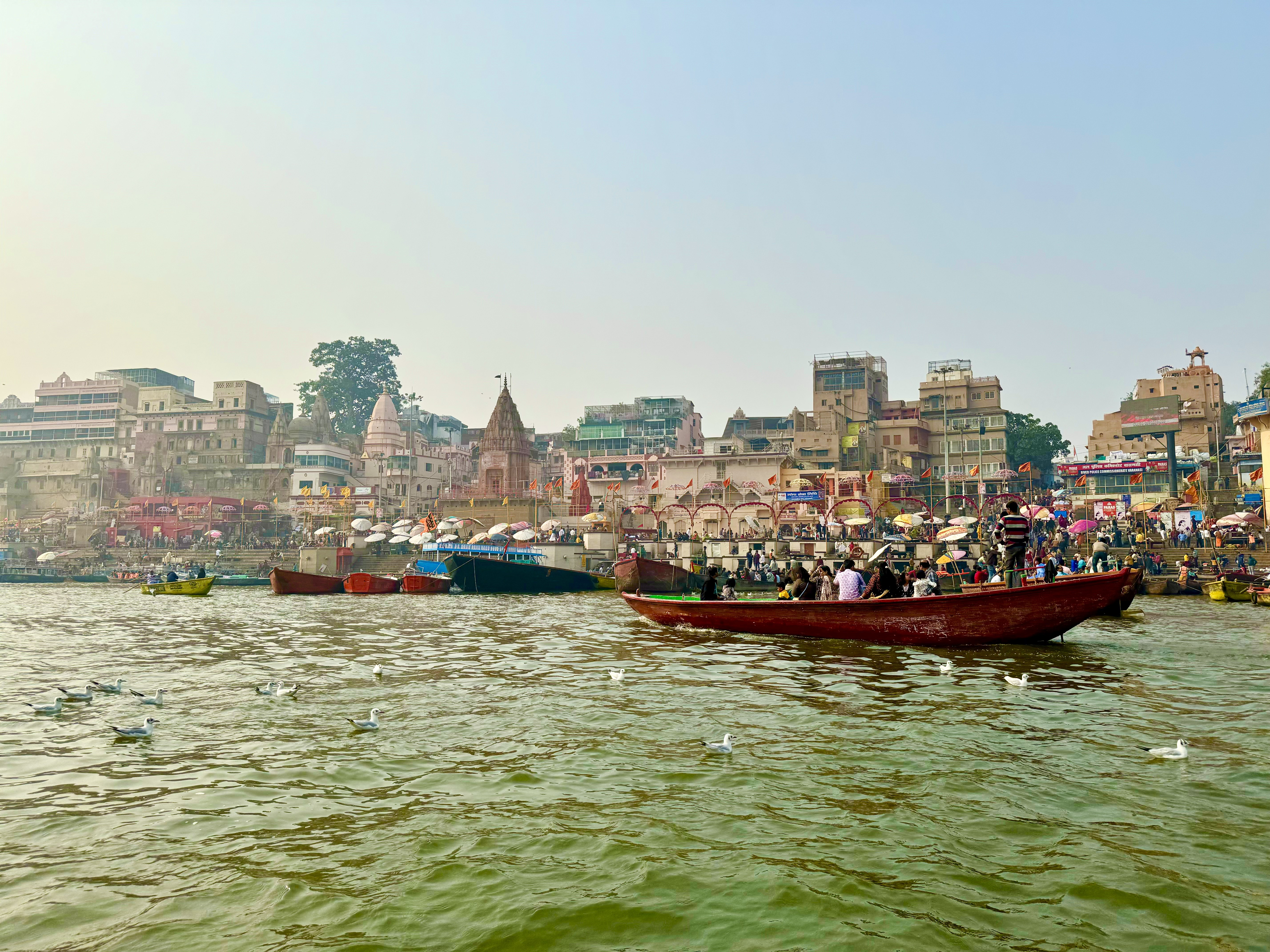 Varanasi ghats along the Ganges in India, with boats, birds, temples, and people along the riverfront