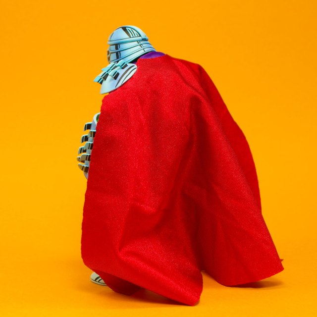 A colorful figure with a red cape, shown from the back against a bright orange background.