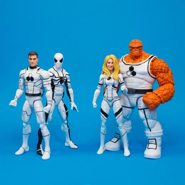 Four action figures posed against a blue background, featuring a male figure in a white suit, a white-suited figure with a black spider emblem, a female figure in a white suit with blonde hair, and an orange, rocky figure.