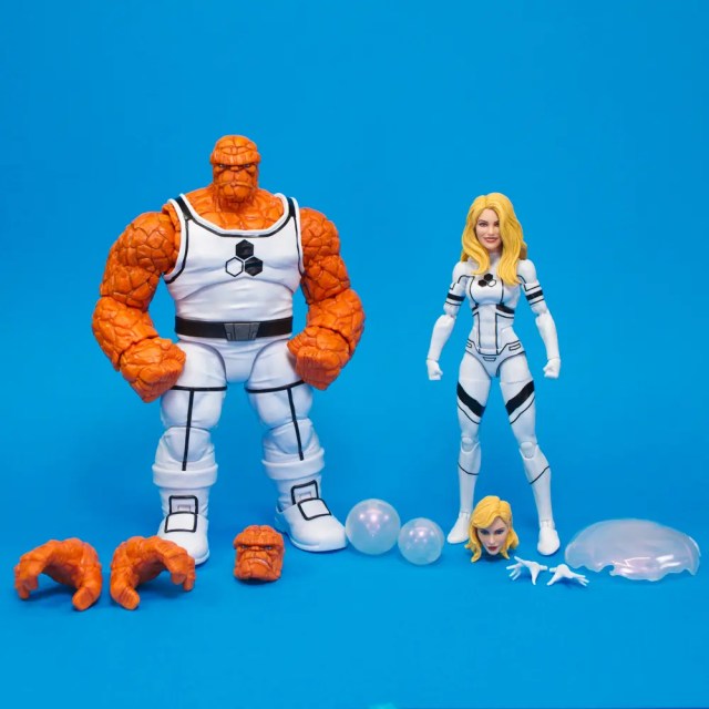 Action figures of The Thing and Invisible Woman from the Fantastic Four, displayed against a blue background, with additional interchangeable parts including alternate hands and heads.