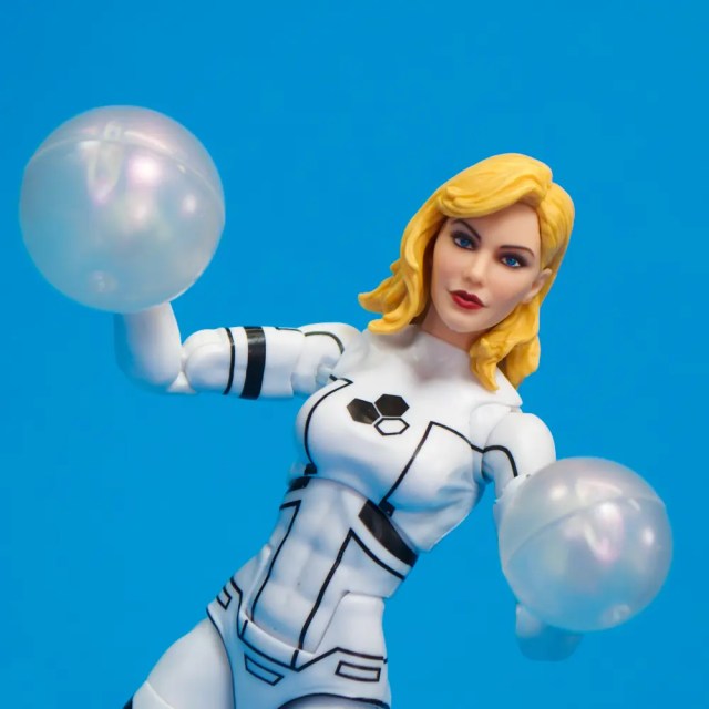 Action figure of a female character in a white and black suit, holding two translucent spheres, against a blue background.