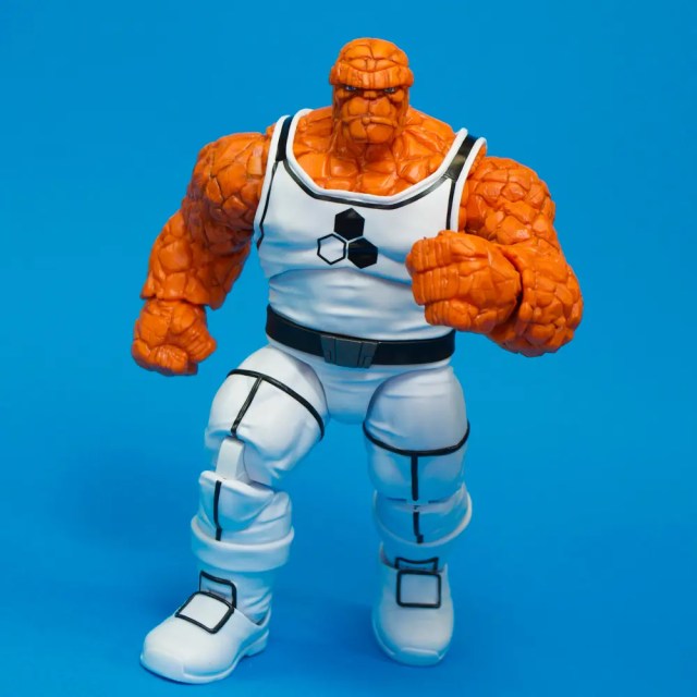 A detailed action figure of a muscular character with an orange rocky texture, wearing a white outfit with black accents, standing against a blue background.