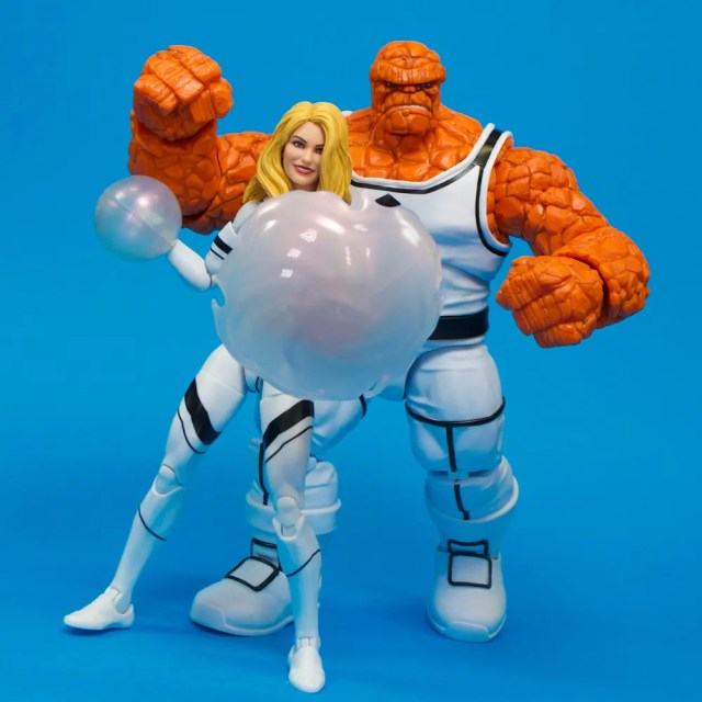 Two collectible action figures on a blue background: one features a female character with long blonde hair and a bubble, while the other is a muscular orange figure with a textured appearance.